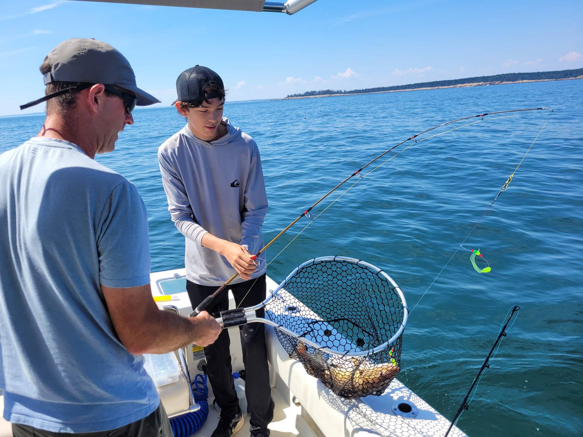 a man holding a fish in a boat on the water in Maine