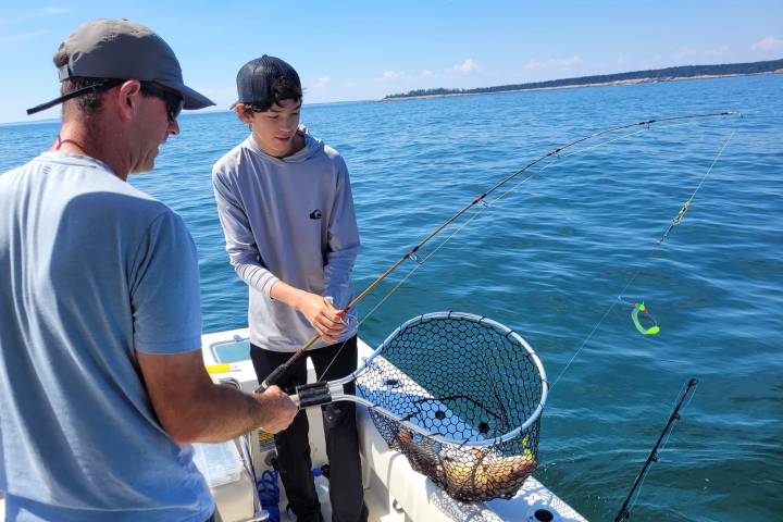 a man holding a fish in a boat on the water in Maine