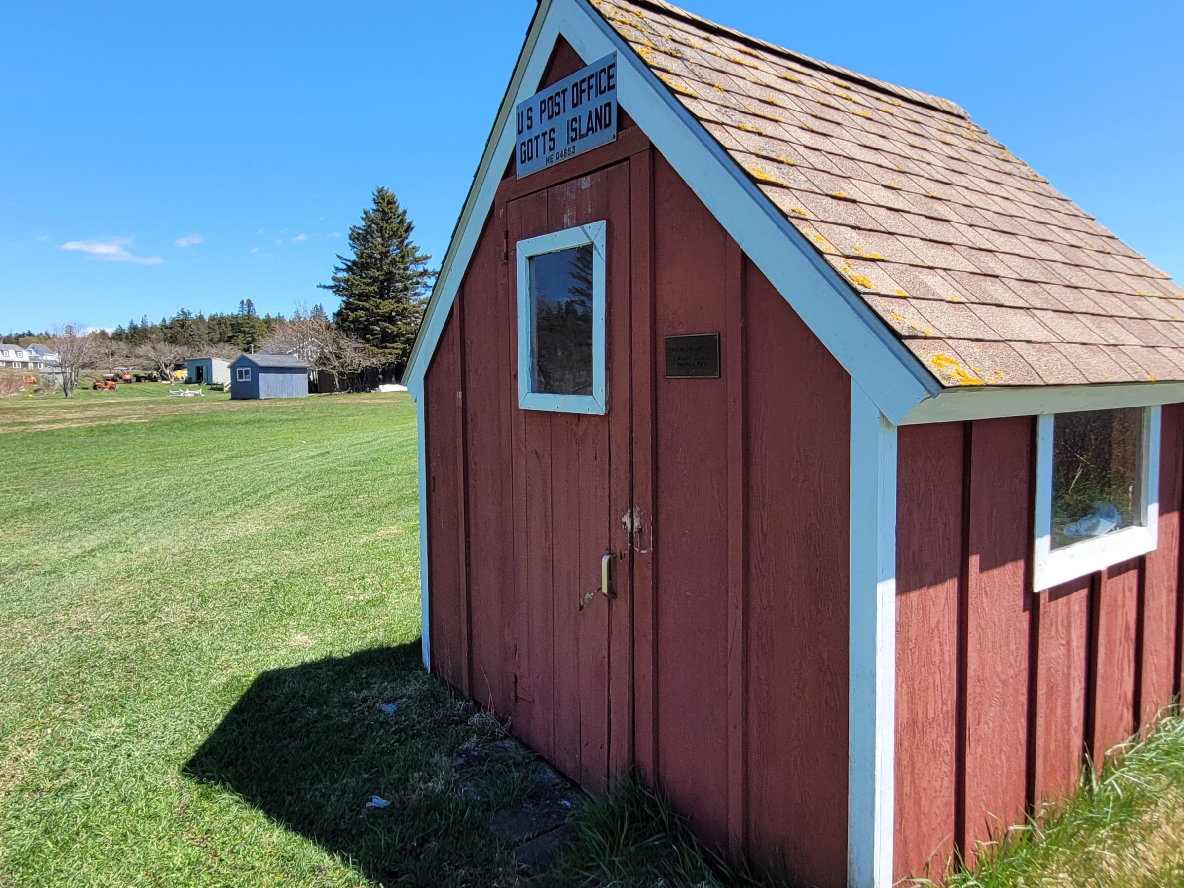 Small red post office building on a grassy field under a clear blue sky.
