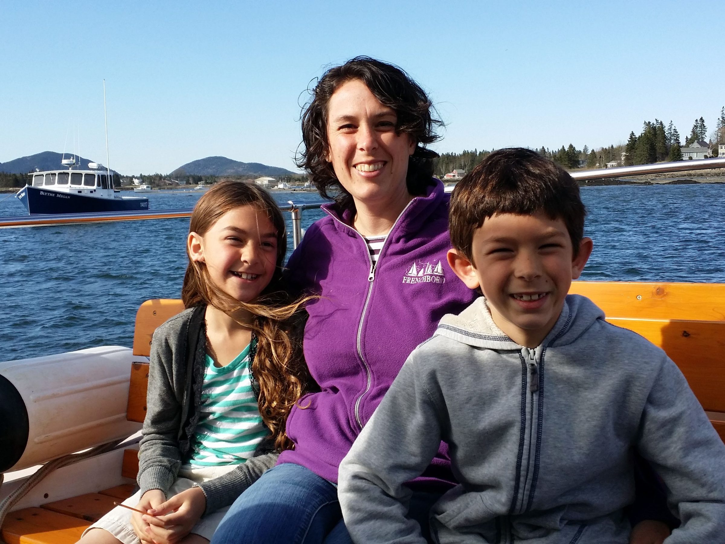 Three people smiling on a boat with water and mountains in the background.