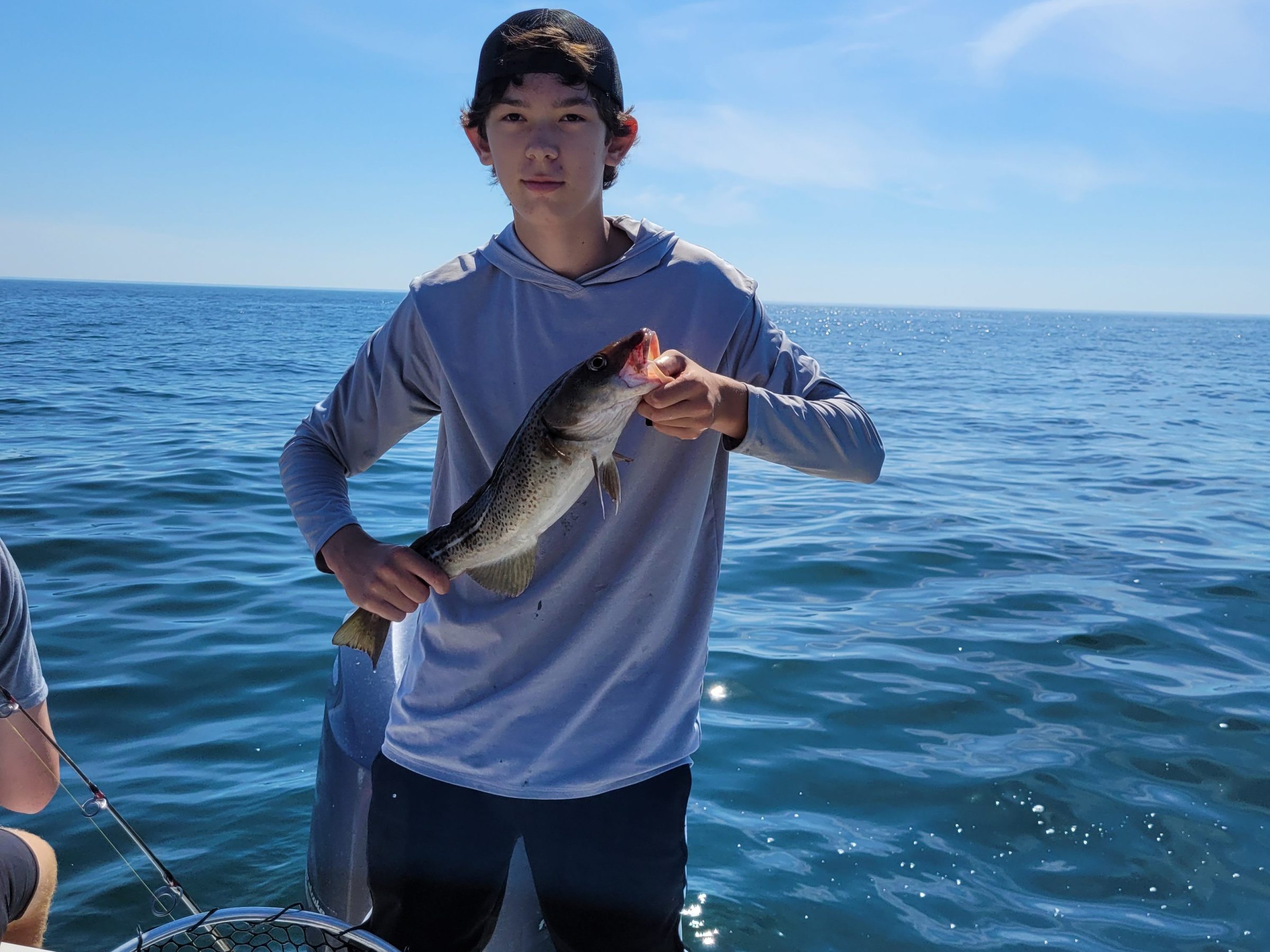 Person holding a fish on a boat with ocean in the background.