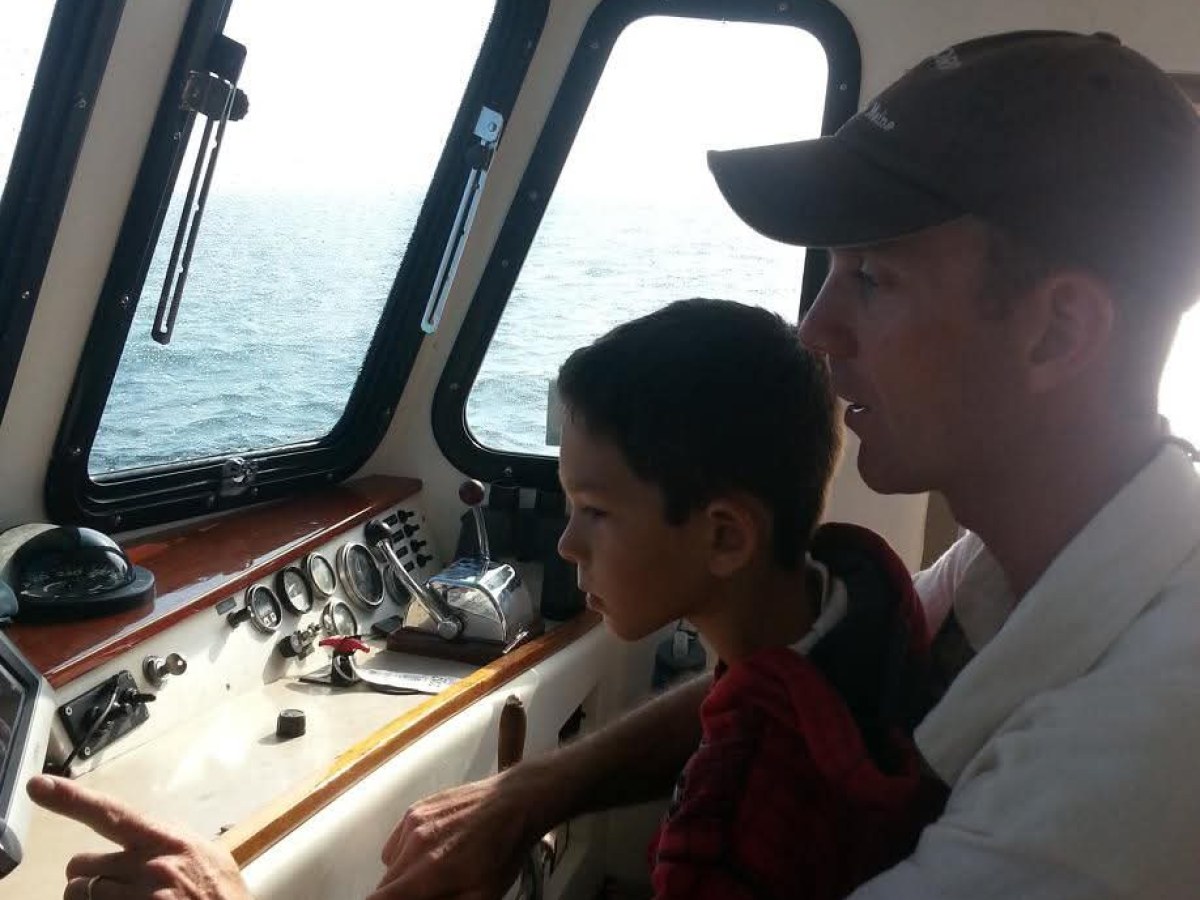 Adult and child navigating a boat together, looking at controls.