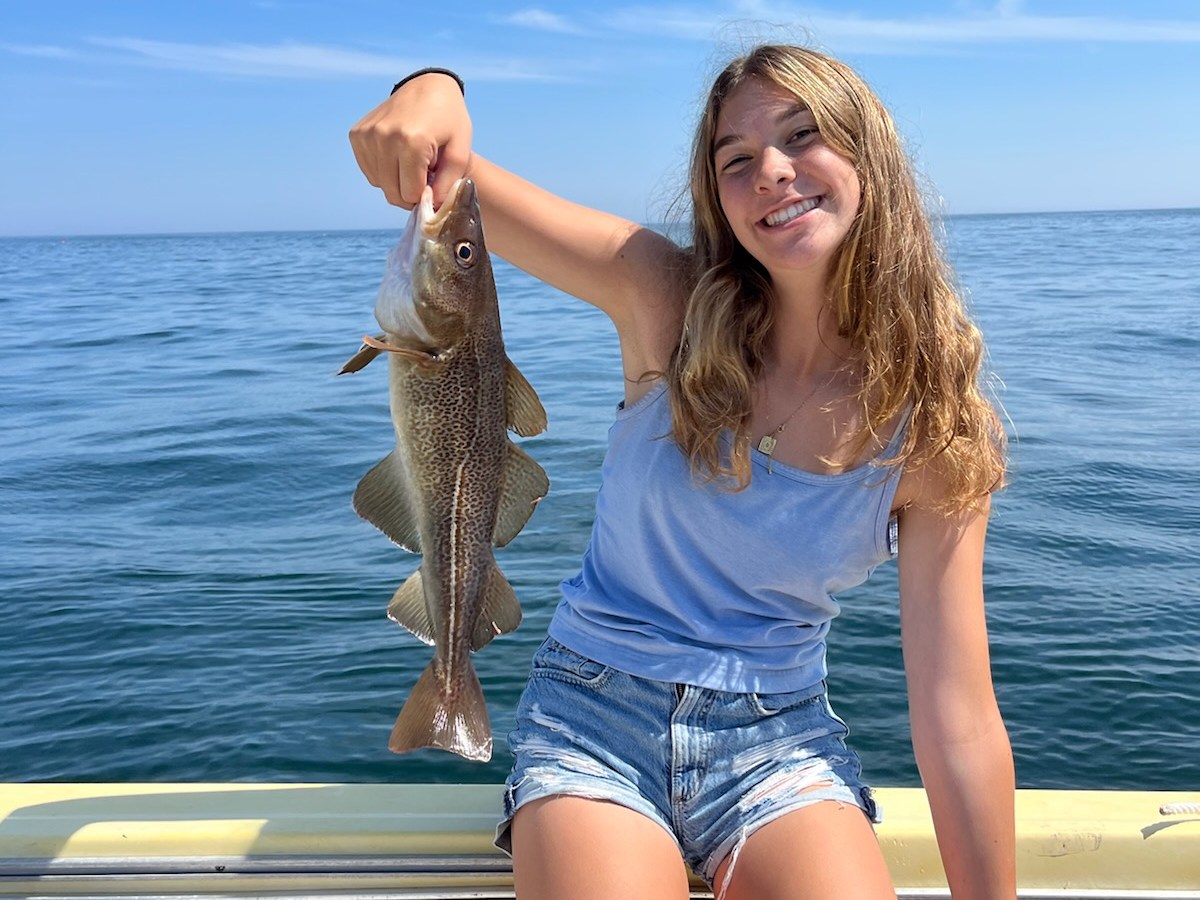 Person holding a fish on a boat with the ocean in the background.