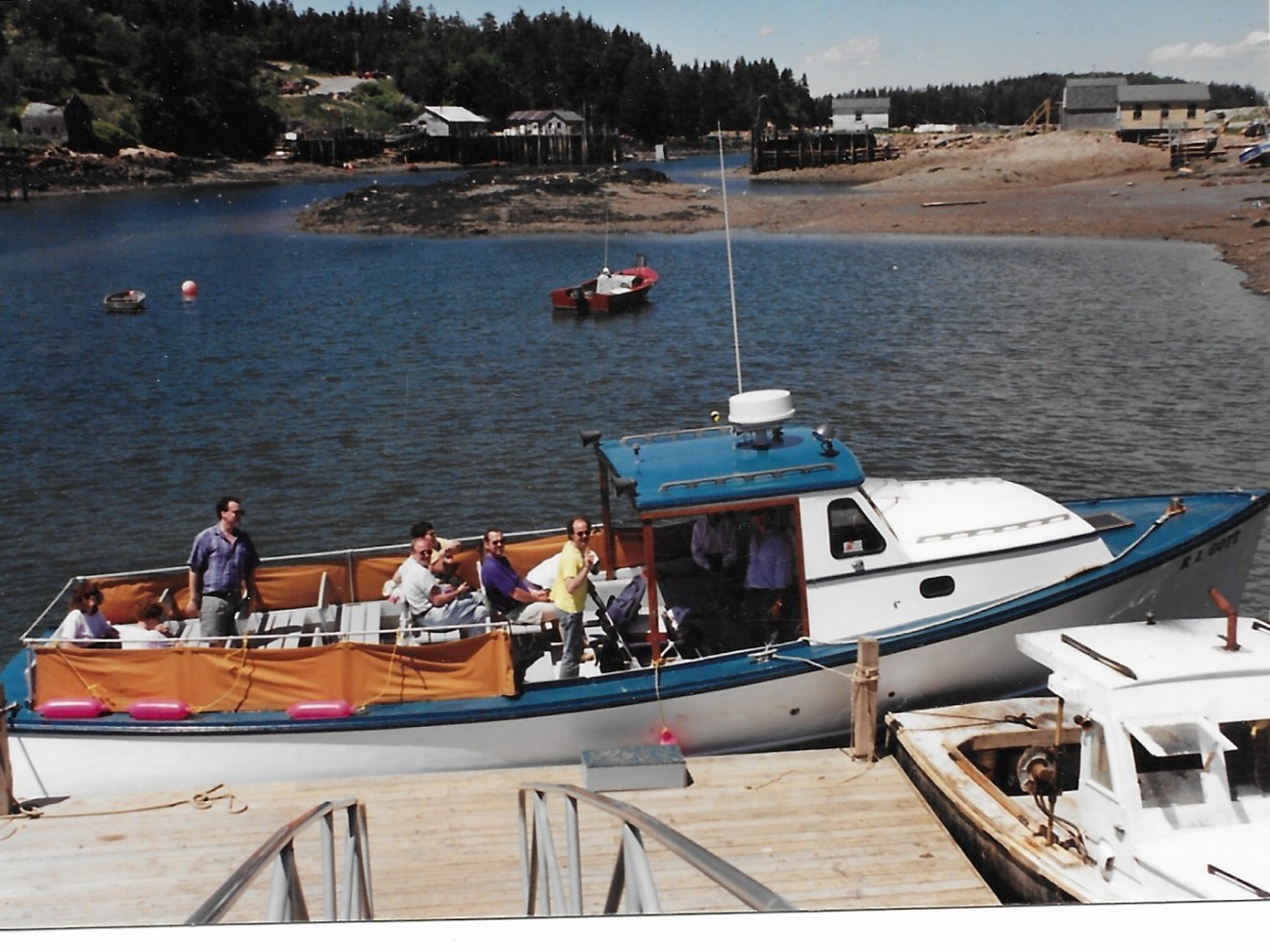 People in a boat docked by a wooden pier on a calm lake.